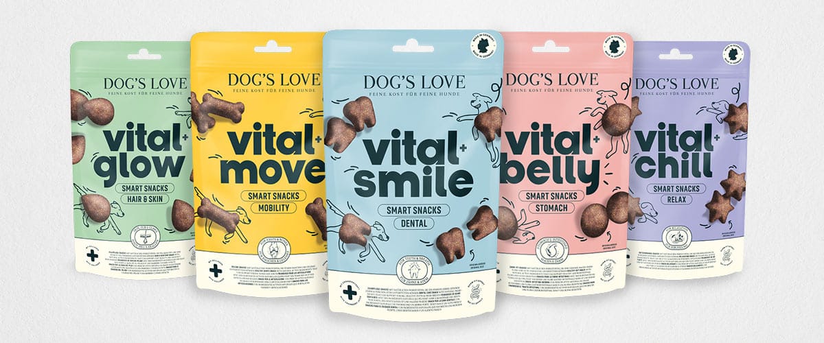 Das Bild zeigt eine Reihe von Hundesnacks der Marke „Dog's Love“ mit dem Namen „Vital Snacks“. Fünf verschiedene Verpackungen in Pastellfarben präsentieren die Sorten „Vital Move“ (Gelb, für Mobilität), „Vital Glow“ (Grün, für Fell und Haut), „Vital Belly“ (Rosa, für Magen und Darm), „Vital Smile“ (Blau, für Zahnpflege), und „Vital Chill“ (Lila, für Entspannung). Jede Verpackung ist mit Illustrationen und einem minimalistischen Design versehen.