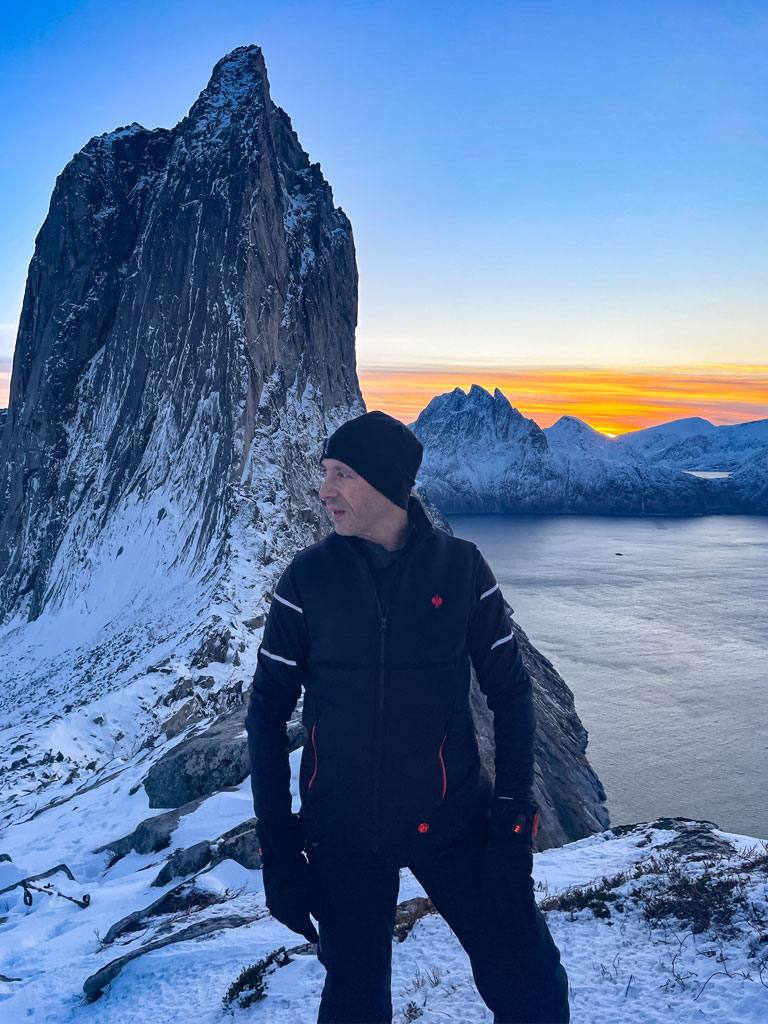 Mann trägt Engelbert Strauss Heizweste auf einem Berg in Norwegen, hinter ihm sind ein Gipfel und ein Fjord zu sehen.